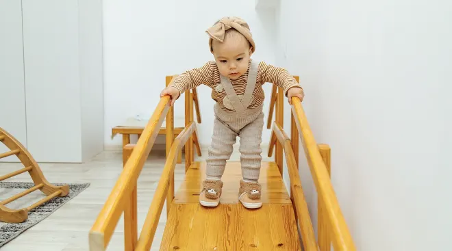 toddler girl climbing on wooden toy at home