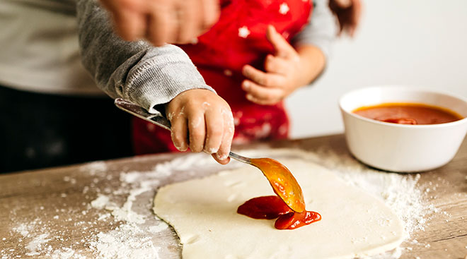 adult helping toddler cook pizza in the kitchen