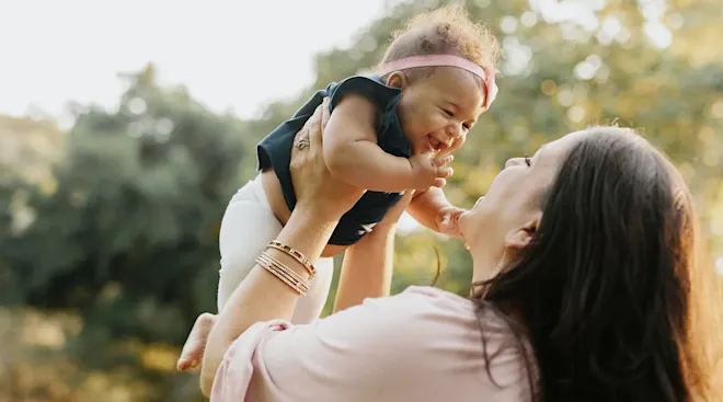 mom holding laughing baby outside
