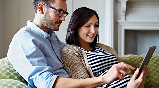 pregnant woman and her partner looking at tablet screen
