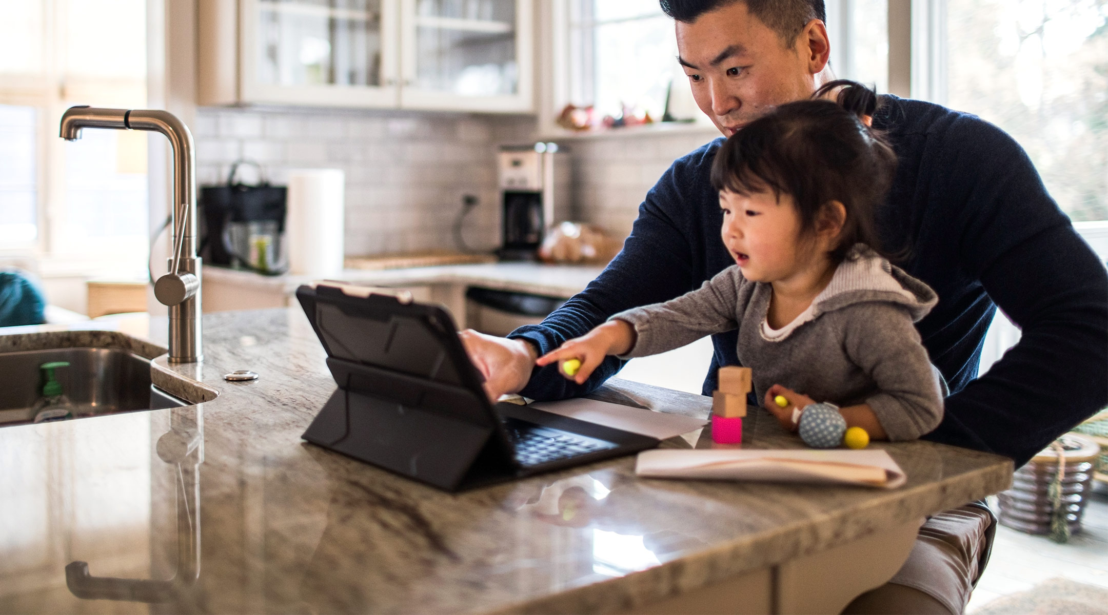 dad working from home with toddler daughter in his lap