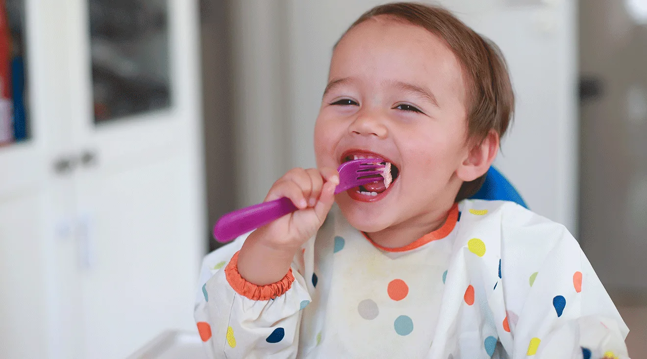 happy toddler eating with fork