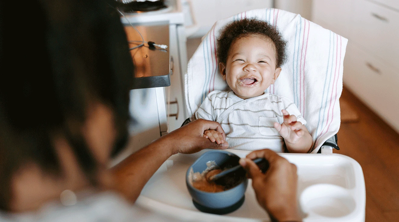 mother feeding laughing baby in high chair