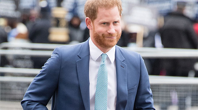 Prince Harry smiling and walking in a suit. 