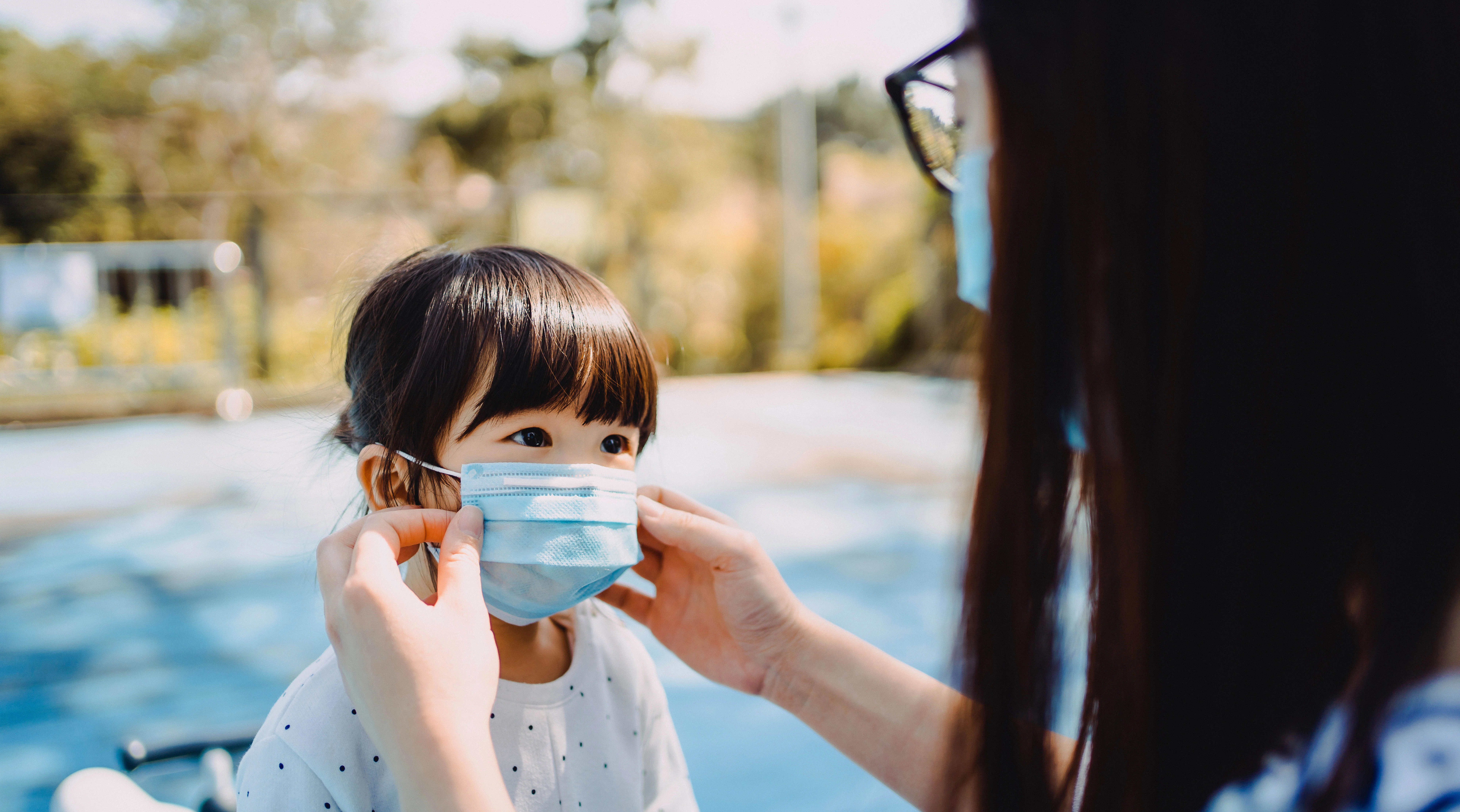 adult helps child put mask on outside