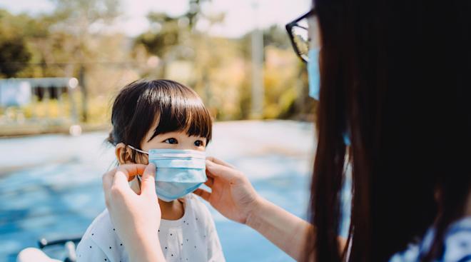 adult helps child put mask on outside