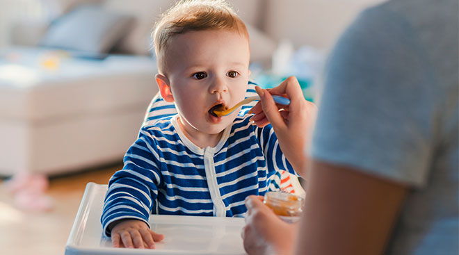 Parent feeding baby spoonful of baby food while baby his its mouth open.