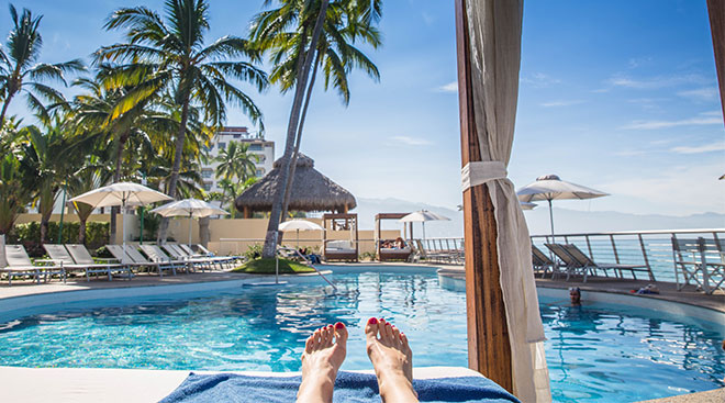 View of beach resort pool and woman's feet relaxing in her cabana.