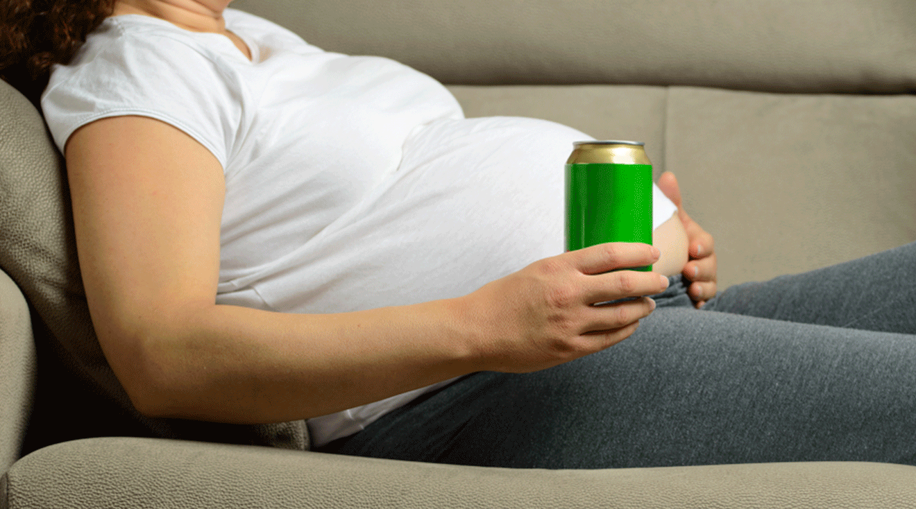 pregnant woman holding a canned drink while sitting on sofa at home