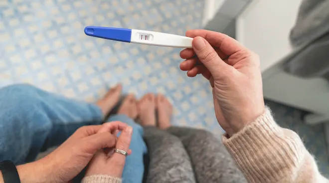 couple holding positive pregnancy test in bathroom at home