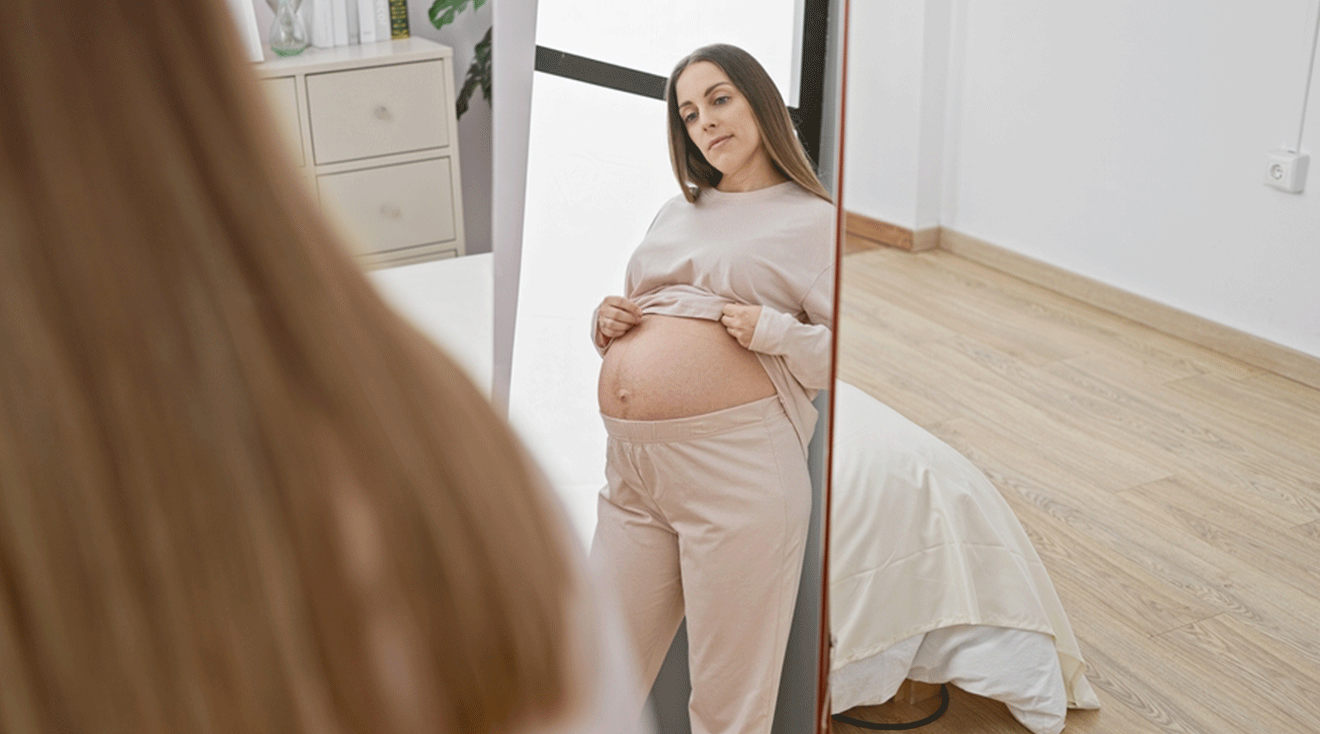 pregnant woman wearing loungewear looking in mirror at home