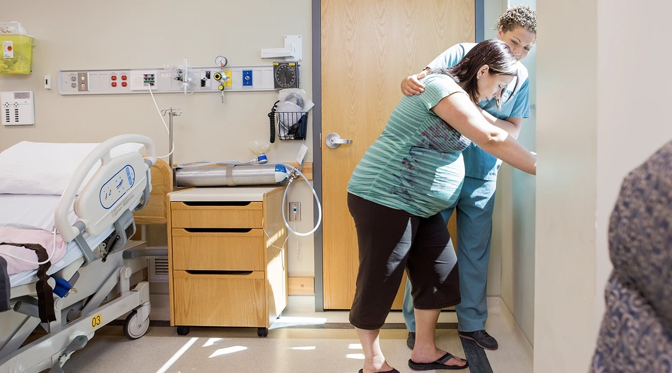 pregnant woman in labor standing in labor and delivery room with mid wife nurse assisting 