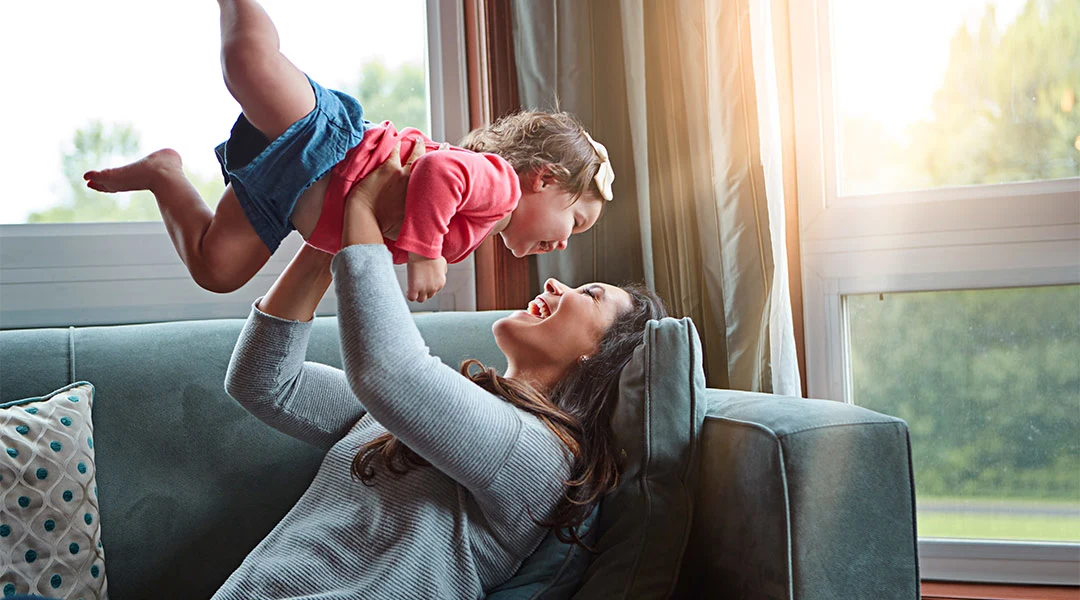 happy mom lifting her daughter into the air while on the couch