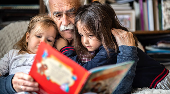 Grandfather sitting with his two grand daughters and reading a book. 