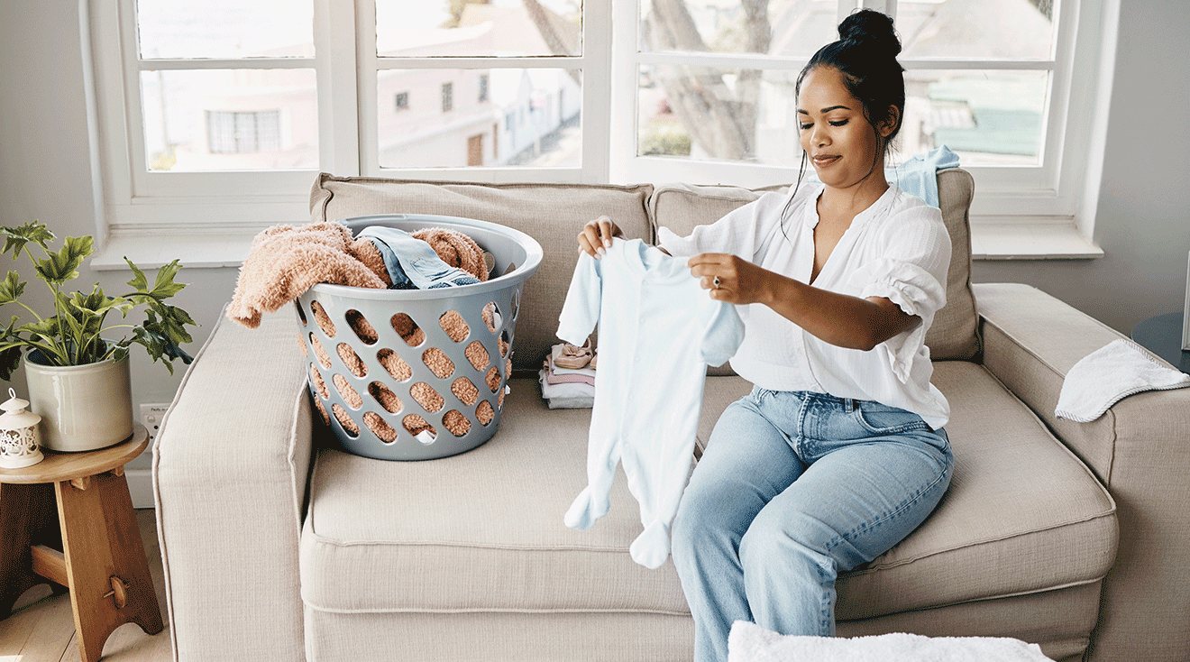 mother folding washed baby clothes at home on the couch