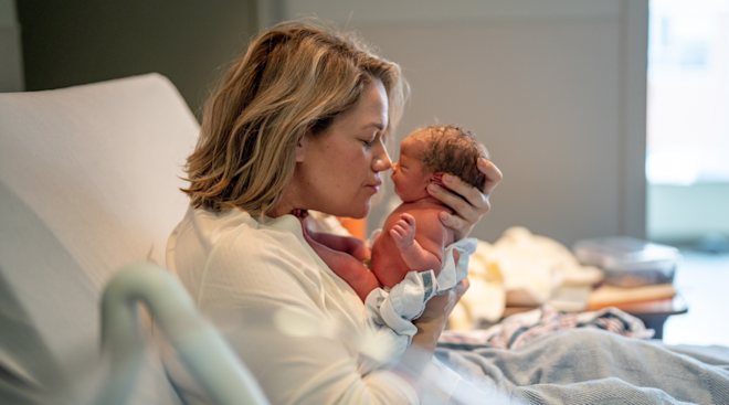 mom in hospital bed snuggling newborn baby