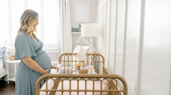 pregnant woman standing beside crib in baby's nursery