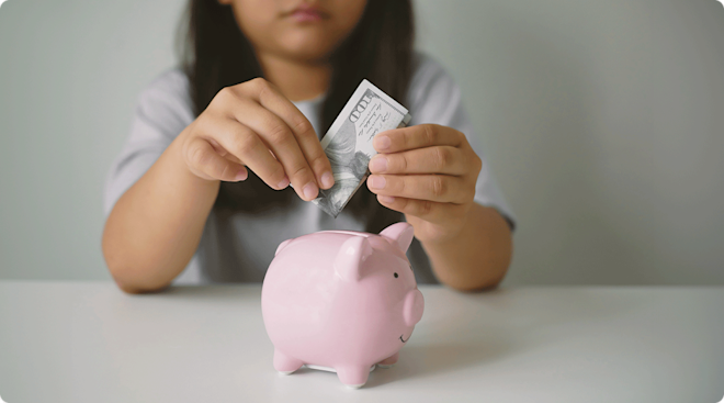 little girl putting money into piggy bank