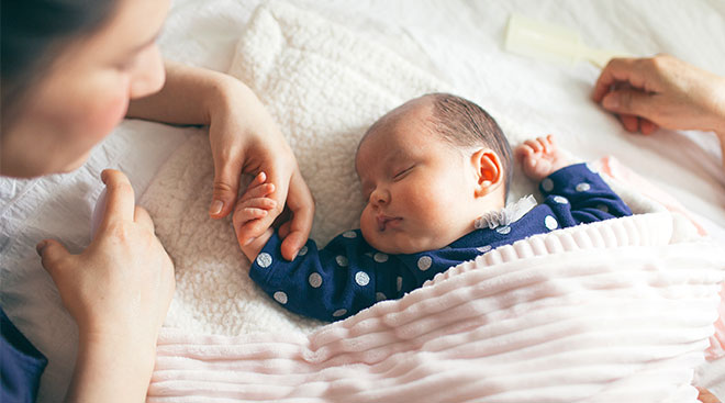 Peaceful new baby sleeping with mom holding its hands. 