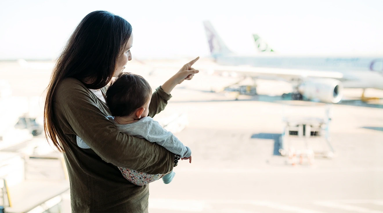 mother holding baby in airport and pointing to airplanes