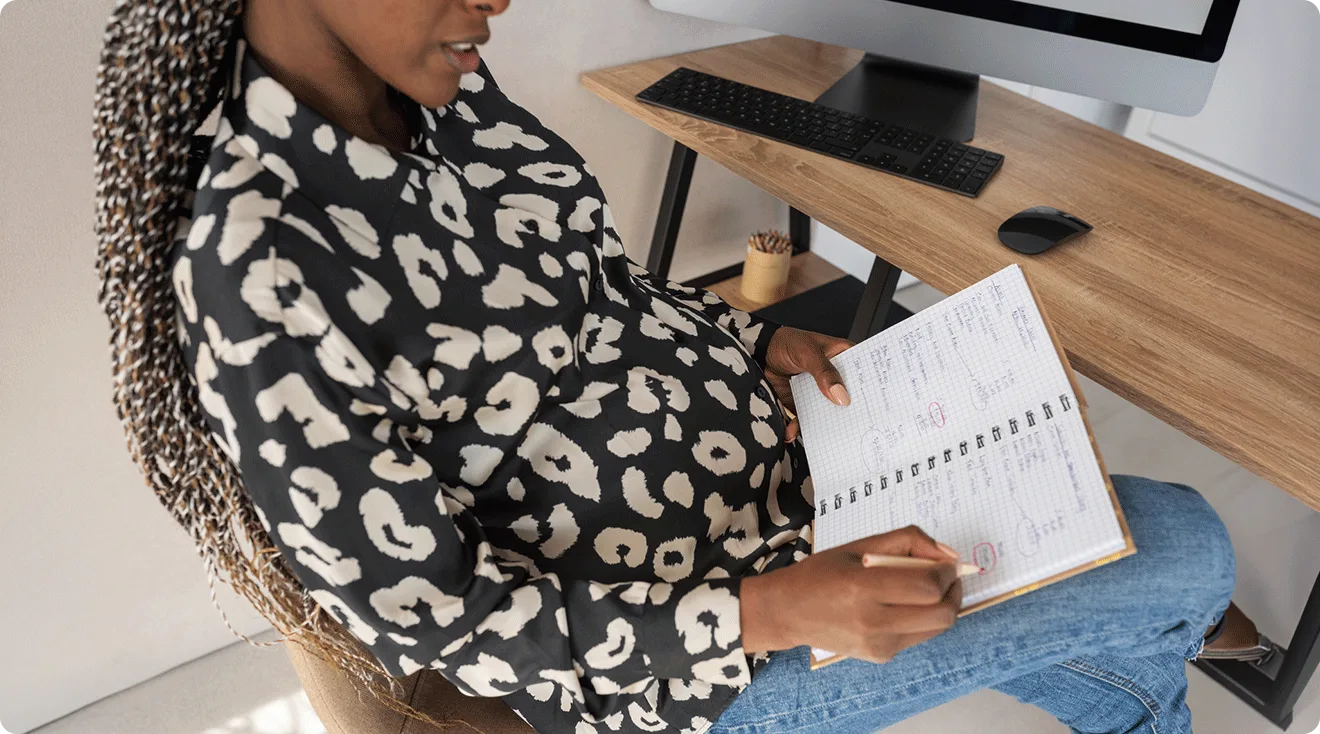 black pregnant woman writing in notebook at desk