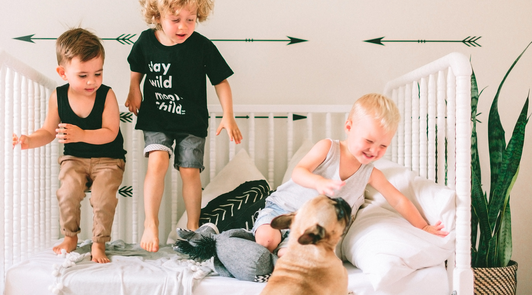 three little boys laughing and jumping on a bed