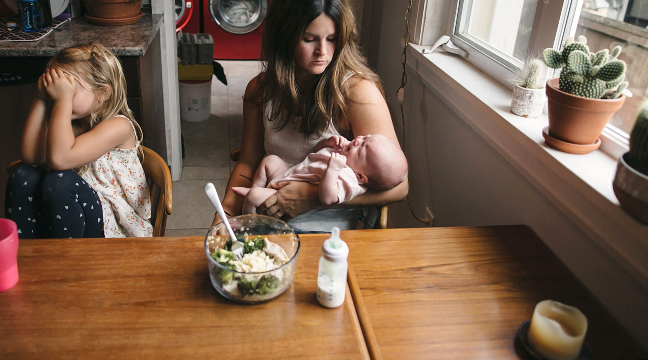 stressed mom with crying baby and child in her kitchen