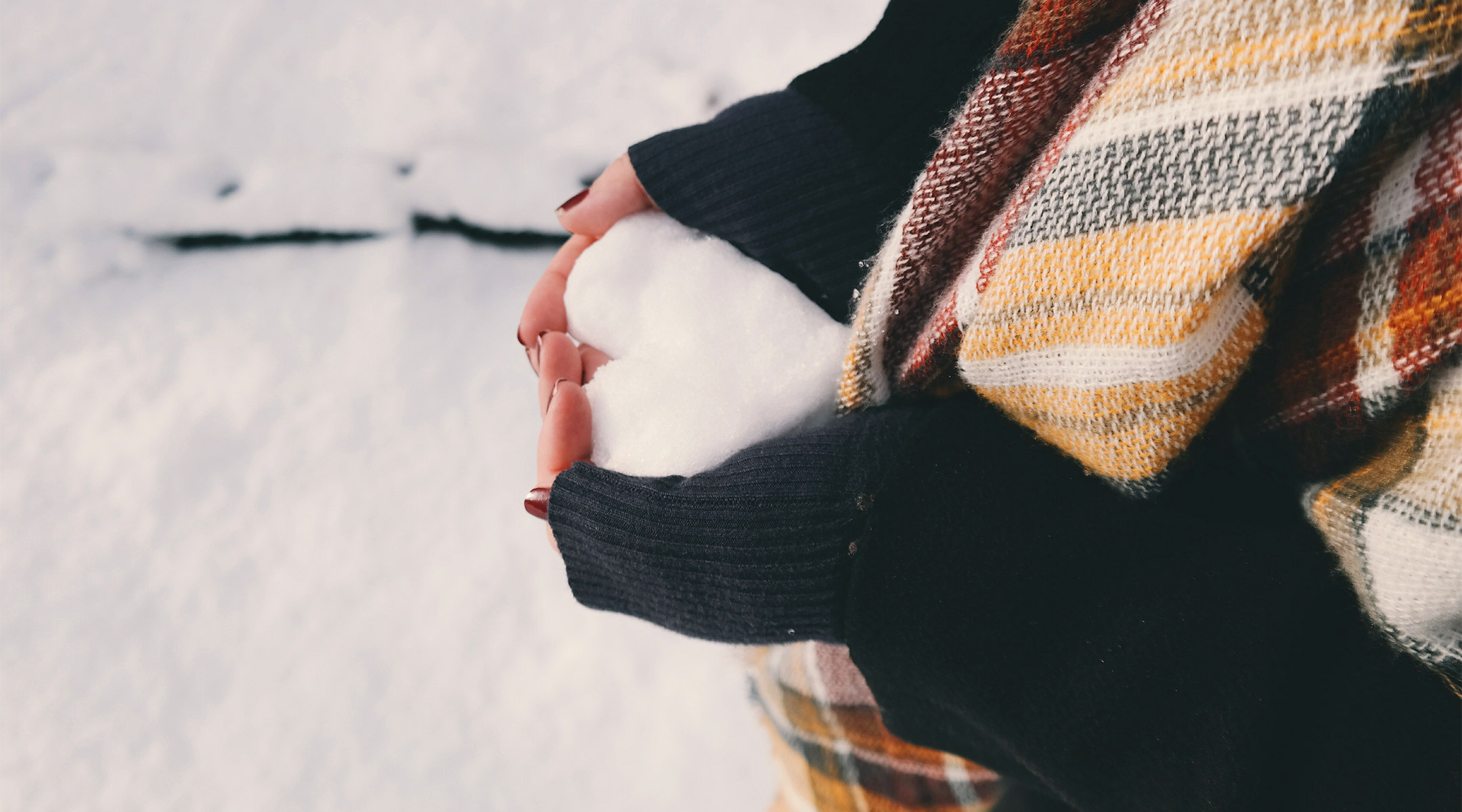 woman holds piece of snow shaped like heart during winter