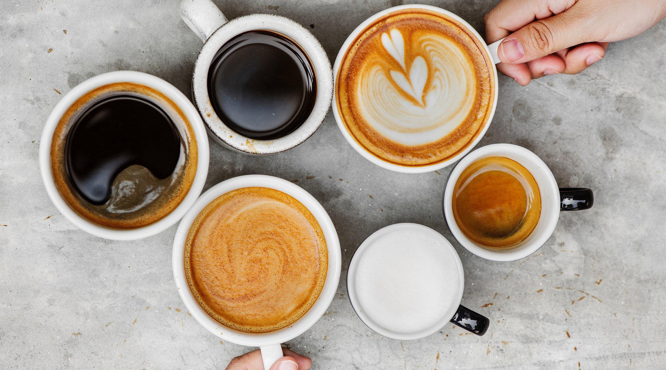 hands with a variety of different kinds of coffee in mugs