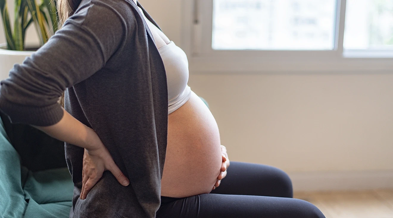 pregnant woman experiencing tailbone pain while sitting on couch at home