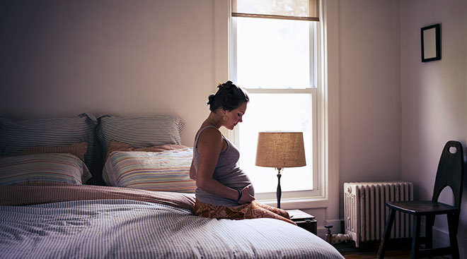 pregnant woman sitting on bed at home thinking