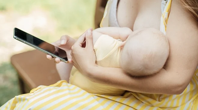 close up of mother looking at smartphone while breastfeeding outside