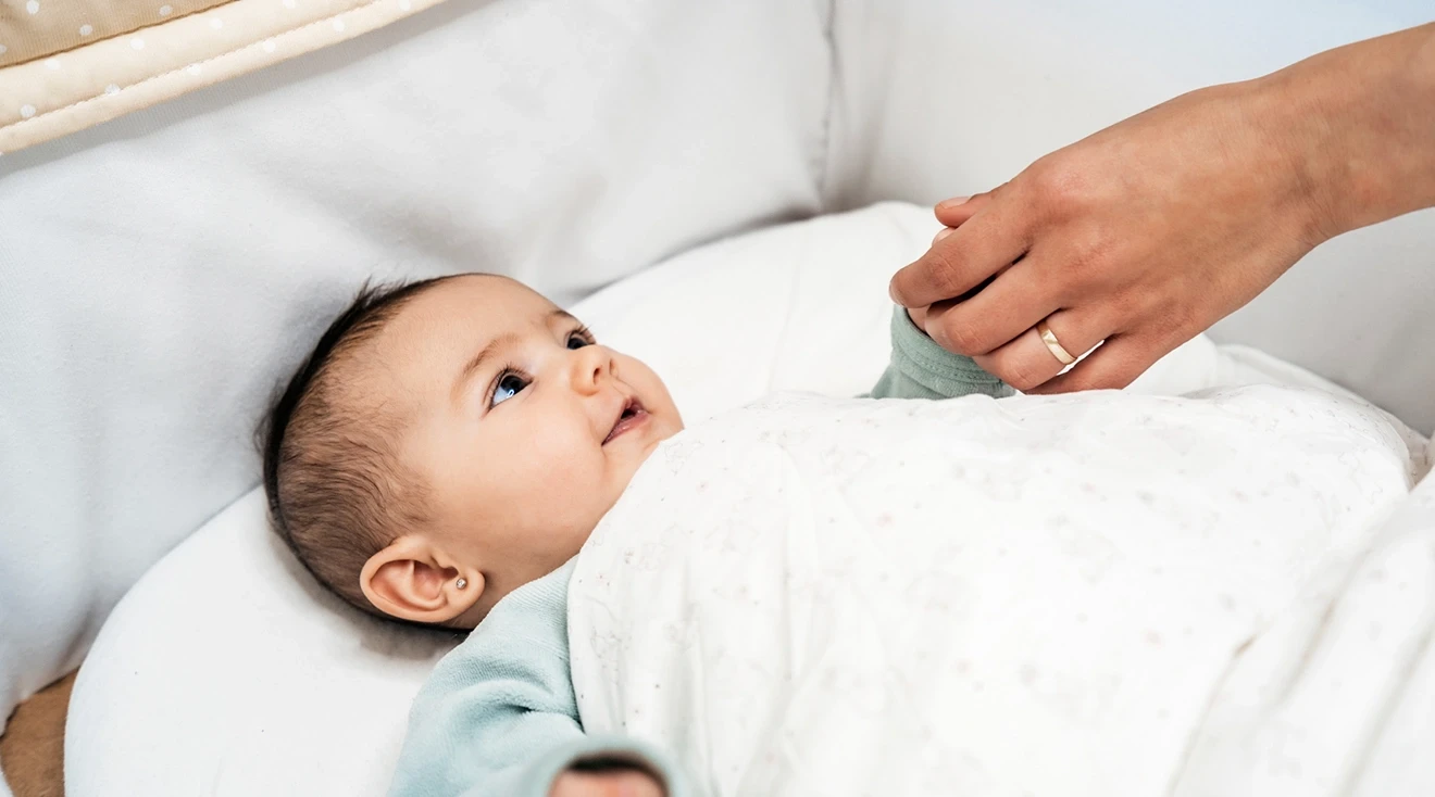 Unrecognizable mother looking at baby girl lying in crib