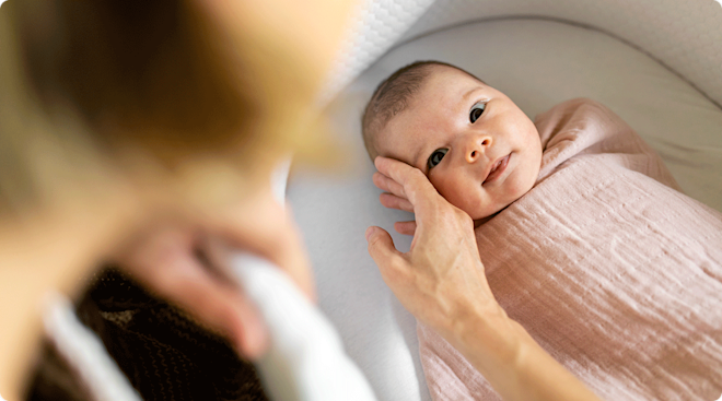 A mother comforting her baby in bassinet.