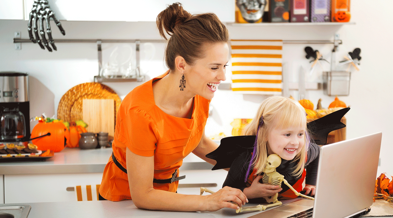 mom and young girl dressed up for halloween while shopping on laptop