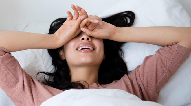 woman in bed covering her face and laughing