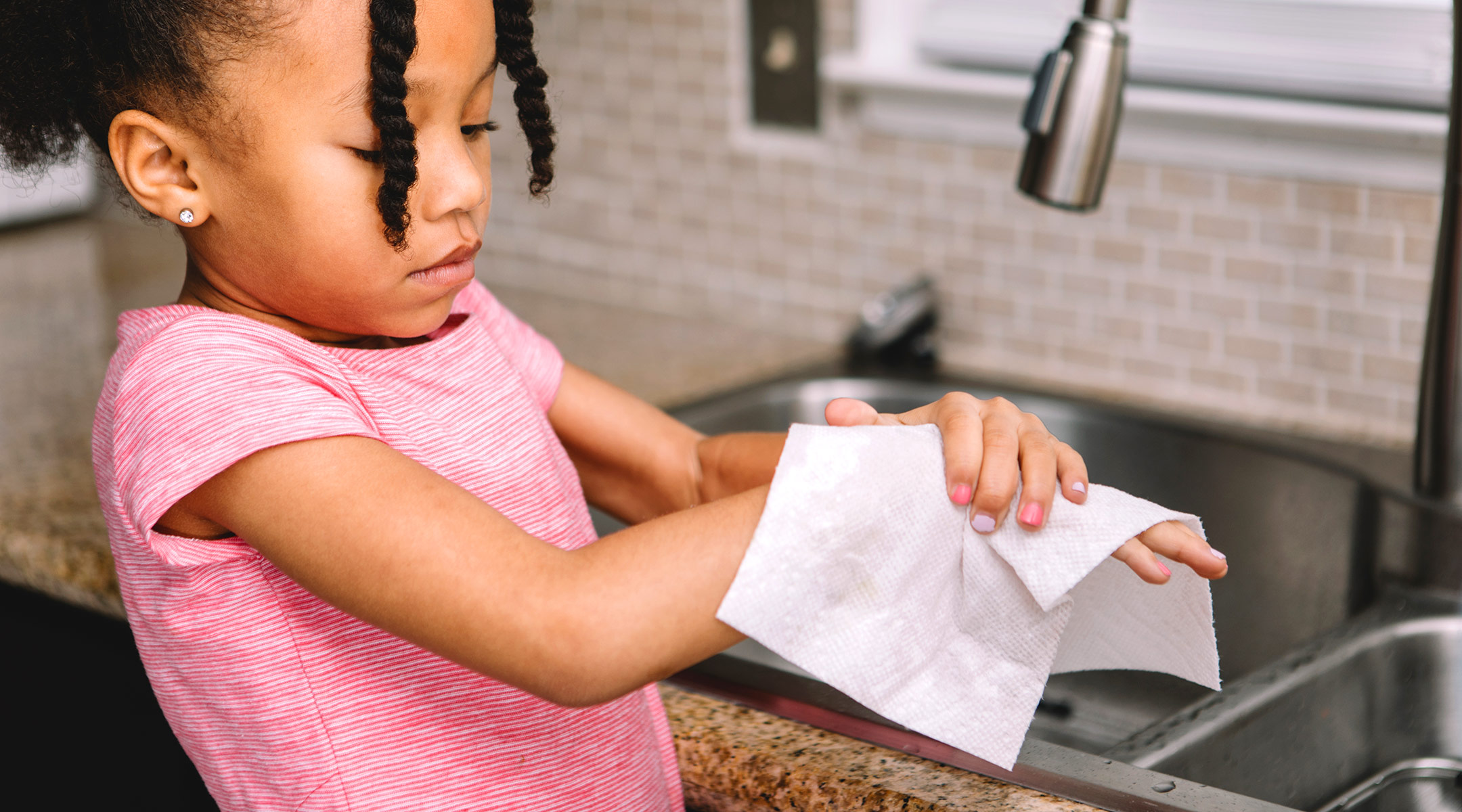 little girl drying her hands after washing them in the kitchen