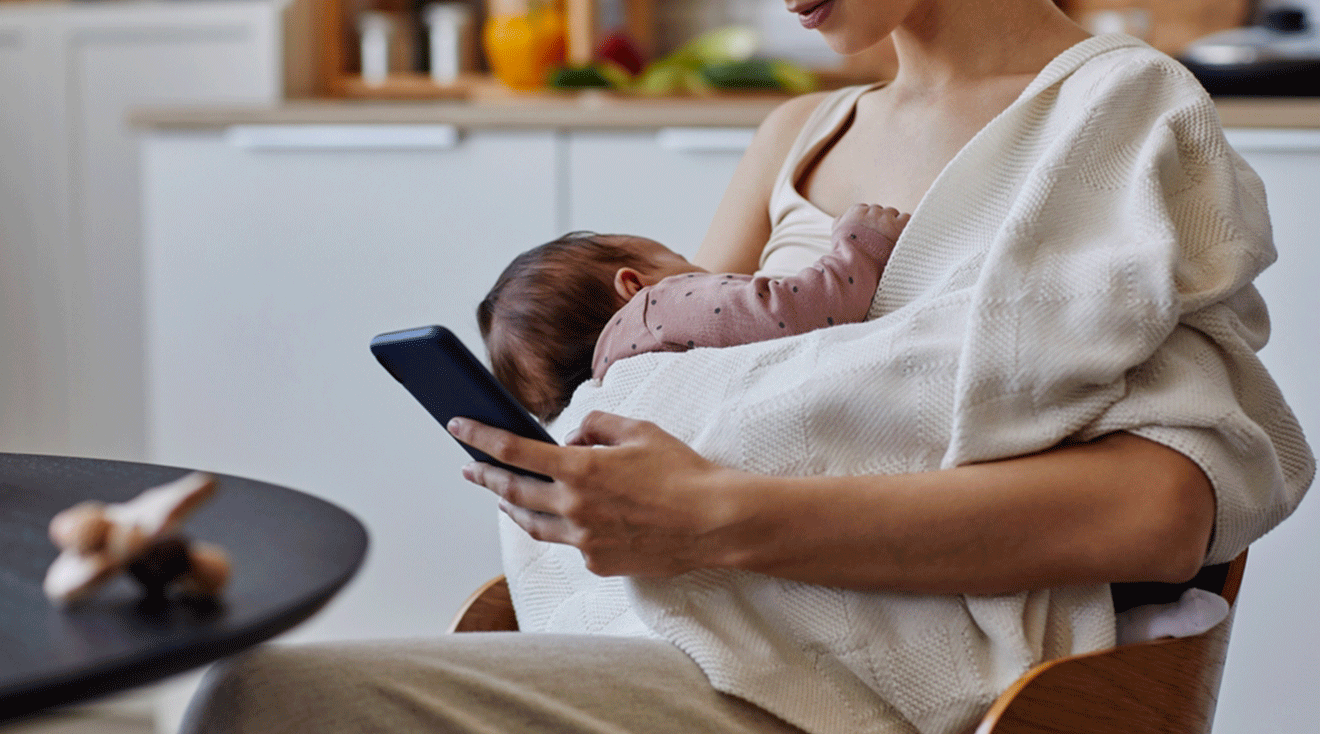 mom looking at social media on smartphone while breastfeeding baby at home