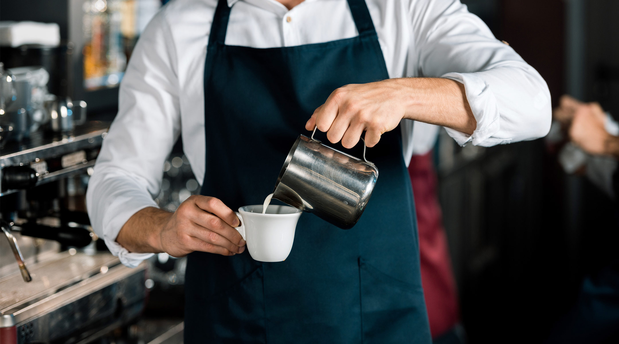 male barista in coffee shop pouring milk into cup