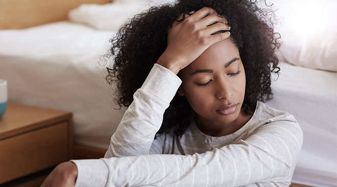 frustrated woman sitting by bed with her hand touching her forehead