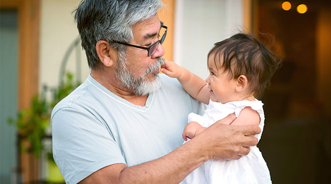 Grandpa holding up his grand baby while she touches his face. 