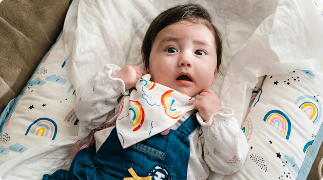 A curious baby wearing a rainbow bib.