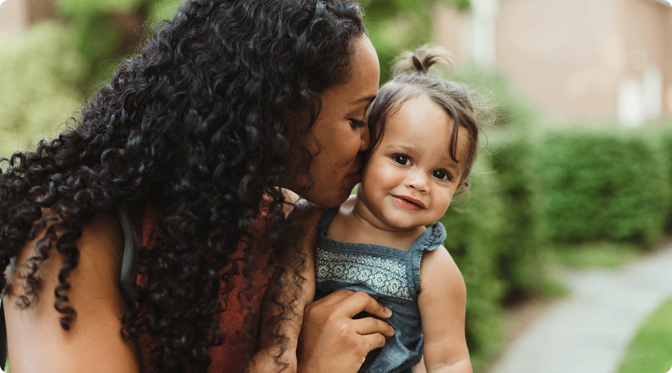 mom kissing baby outside during the summer