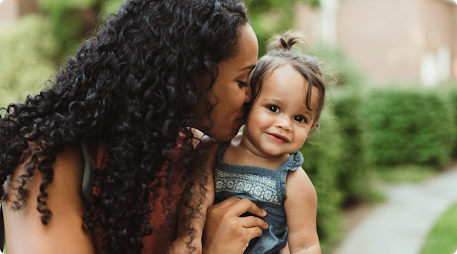 mom kissing baby outside during the summer