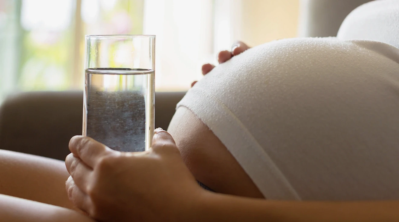 pregnant woman holding a glass of water near belly