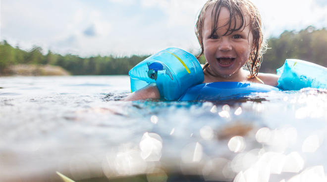 happy toddler swimming in lake with floaties