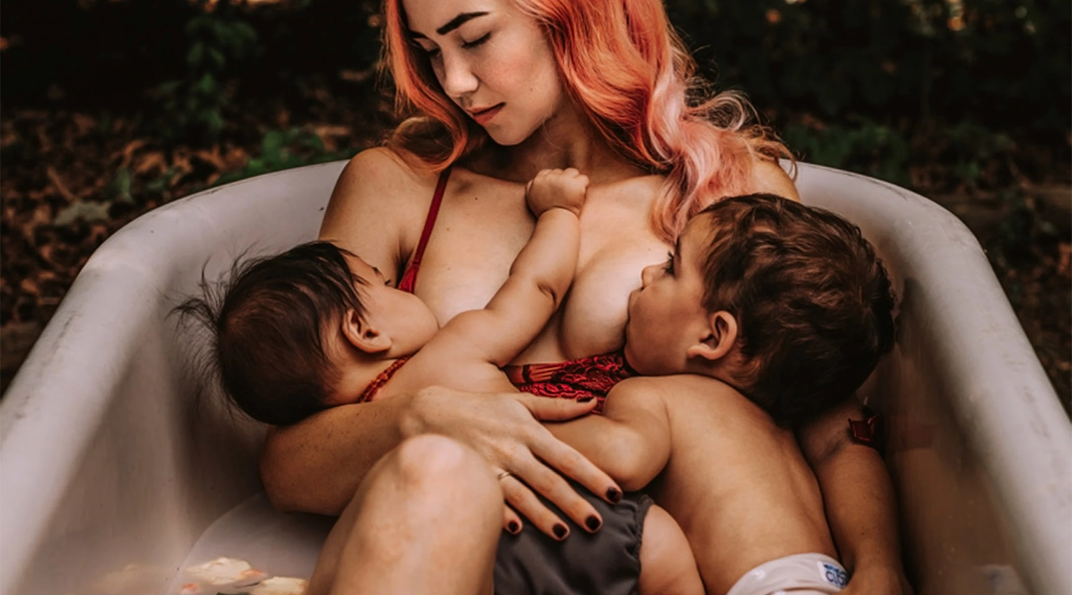 mom tandem breastfeeding siblings in floral milk bath outside