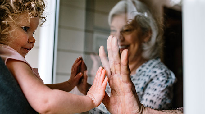 socially distanced grandparent seeing grandchild behind a glass a door 