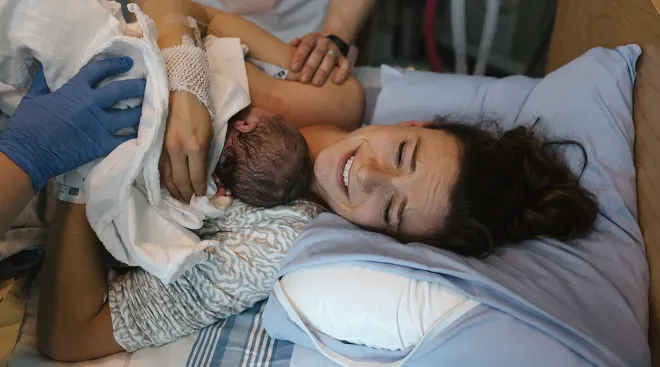 mother who just gave birth holding newborn baby in hospital bed
