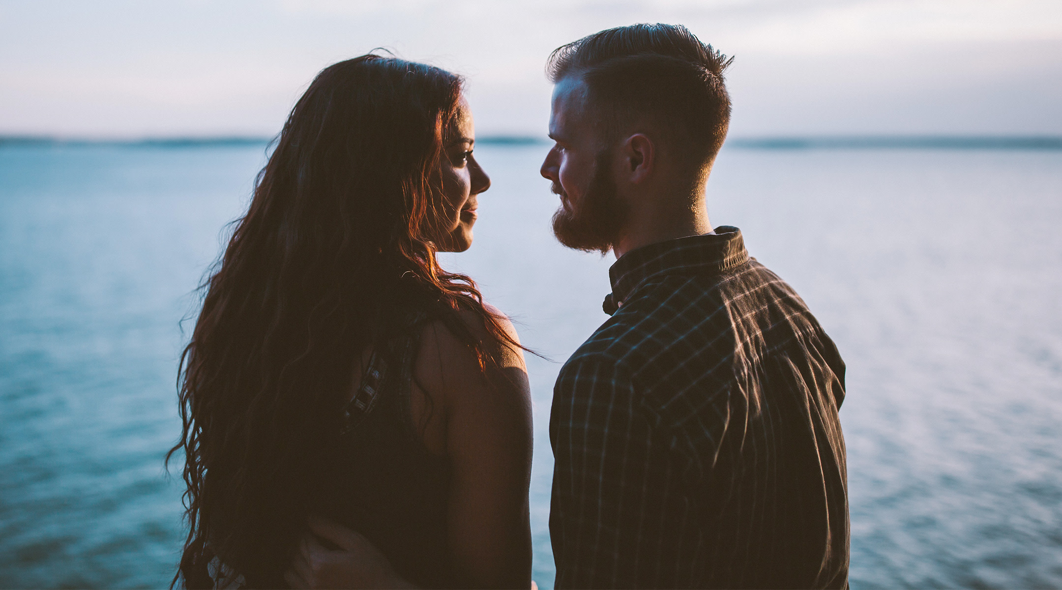 couple gazes into each other's eyes with body of water in the background